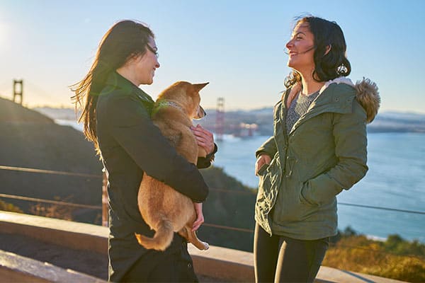 two women smiling and holding a Shiba Inu with San Francisco in the background